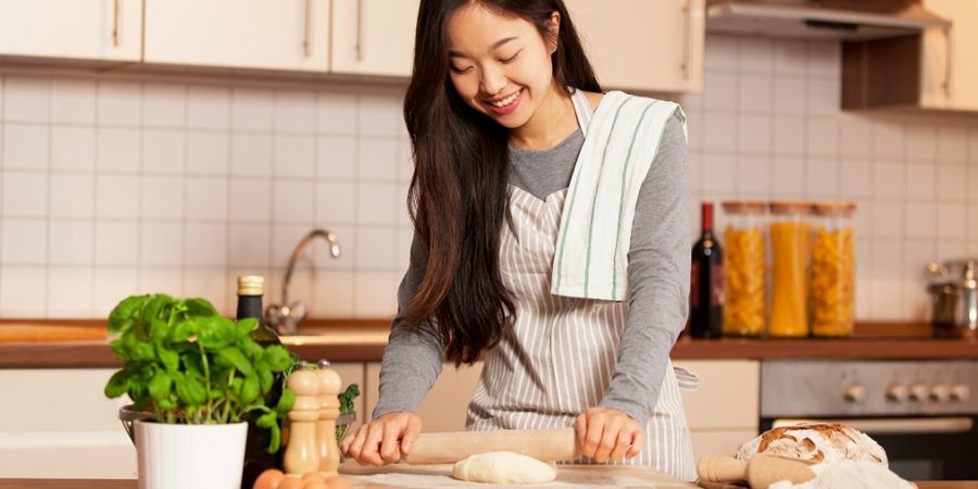 Asian smiling woman is baking bread in her home kitchen