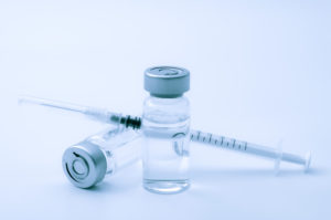 Vaccines, botulinum toxin and insulin ampules concept theme with glass vials with clear liquid next to a syringe and a hypodermic needle isolated on white background