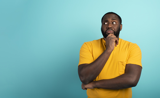 Confused and pensive expression of a black boy with many questions . cyan colored background