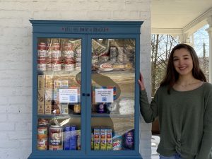 Junior Nora Paladino proudly stands before her Little Free Food Pantry, ready to bring the community together and meet the needs of its members.