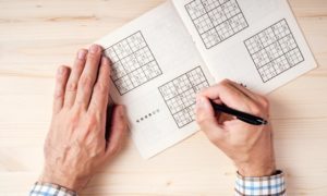 Top view of male hands solving sudoku puzzle on wooden office desk; Shutterstock ID 432200938; Purchase Order: -